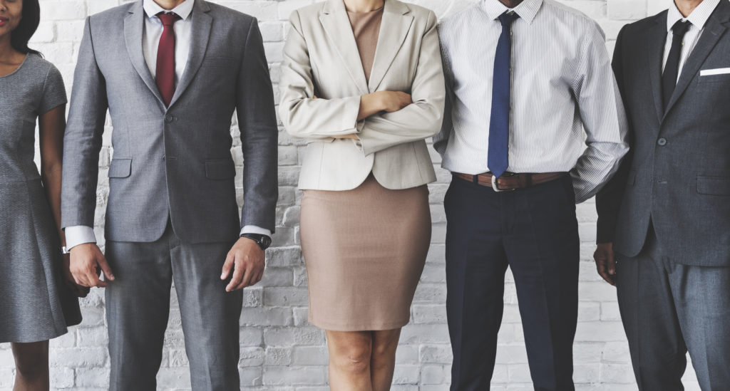 Five well-dressed disability lawyers, three male and two female, are lined up in front of a wall, striking various confident poses.