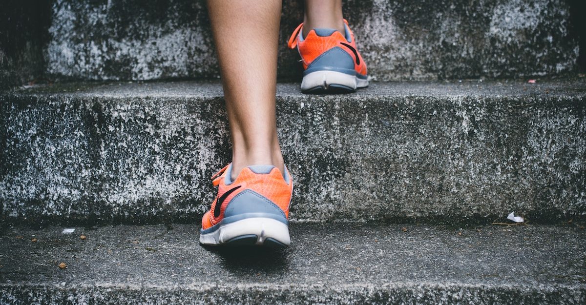 A close-up of a woman's legs climbing stairs, adorned with running shoes. Adidas owes severance pay when an employee is let go.