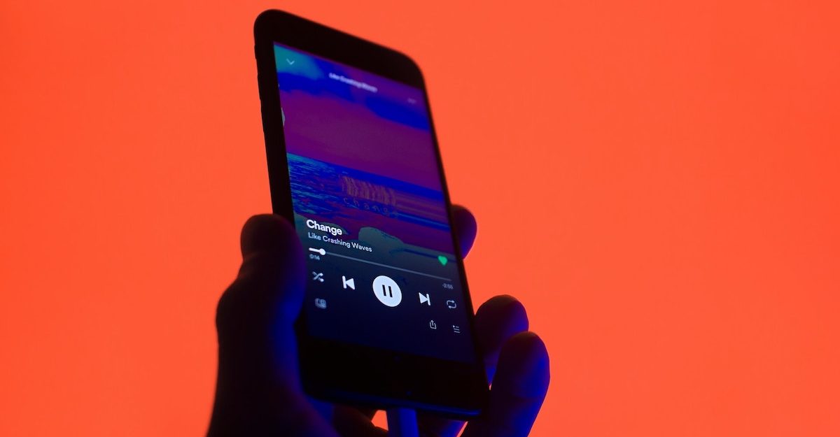 A hand holds up a smartphone that is shown to be playing music, against an orange background. Spotify Canada employees are entitled to severance pay when they lose their job.