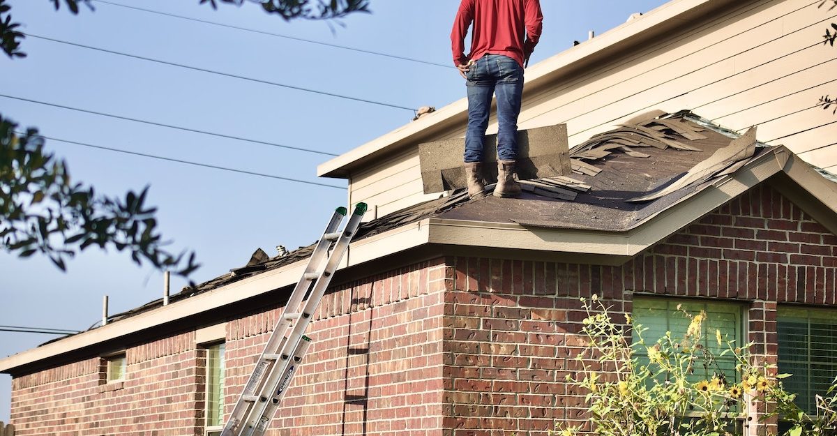 A man in a red sweater is standing on a section of roof that he is in the midst of reshingling. FT Synthetics employees are entitled to severance when they lose their job.