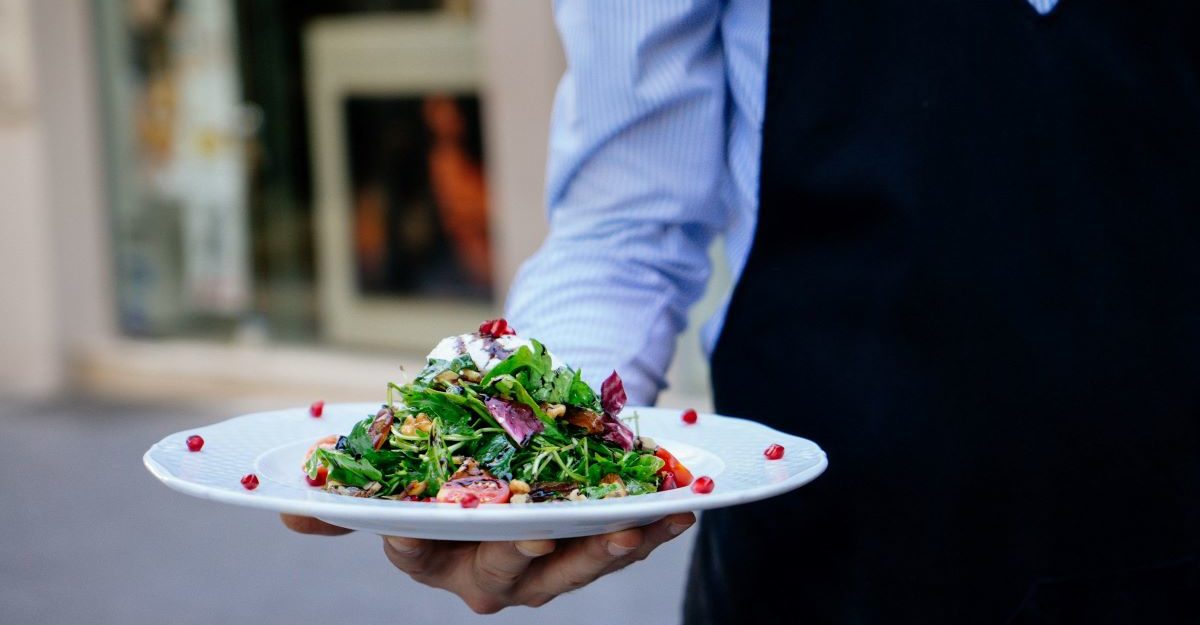 A food server, potentially one provided by Sodexo Canada, holds a plate of food in their hand.