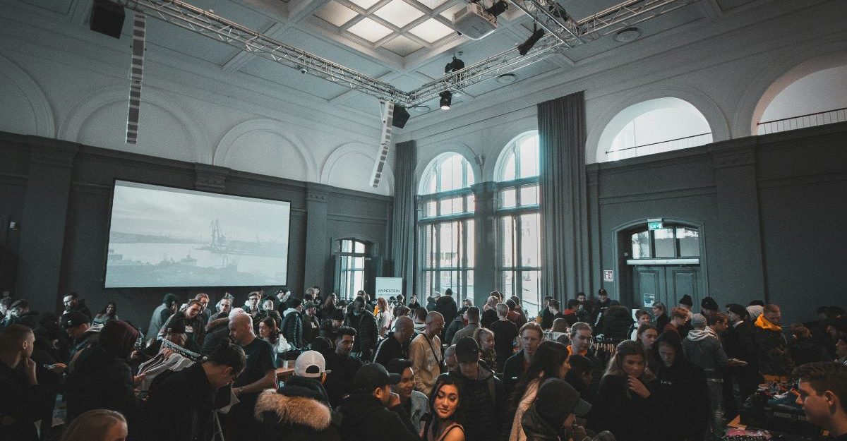 A busy event being held in a large room, complete with overhead lights and large TV, potentially run by Encore Canada.