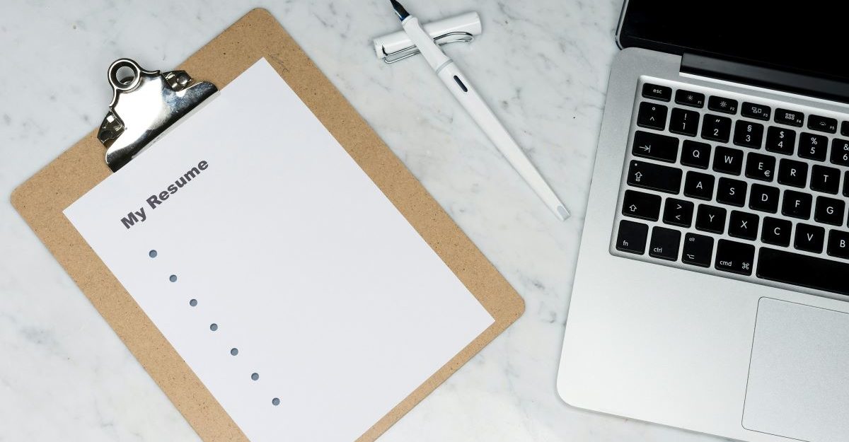 A blank resume lies on a table next to a pen and laptop, perhaps being drafted for review by Procom.