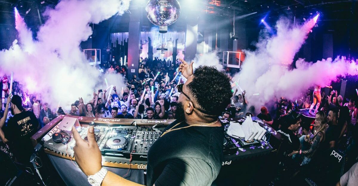 A DJ performs in front of an audience during a live performance at a busy entertainment venue.