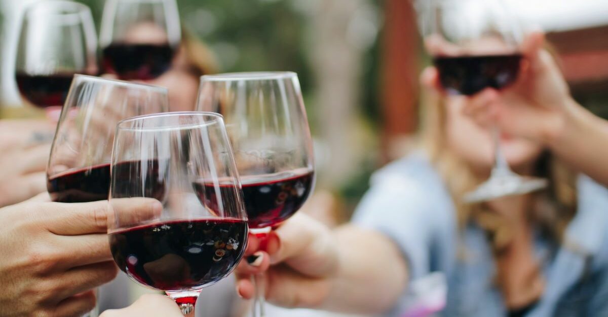 A gathering of people raise clear glasses filled with red wine.