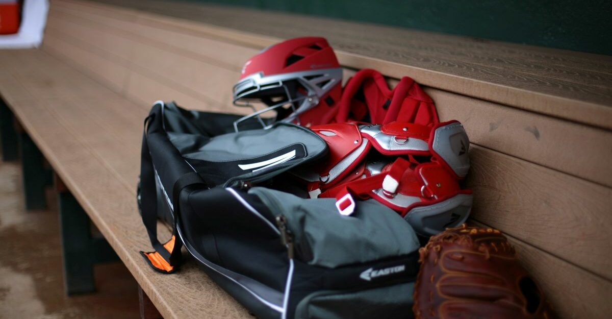 A baseball glove, equipment and duffle bag sit on a dugout bench.