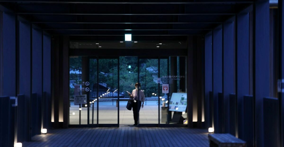 A person walks through automatic sliding doors at the end of a long hallway.