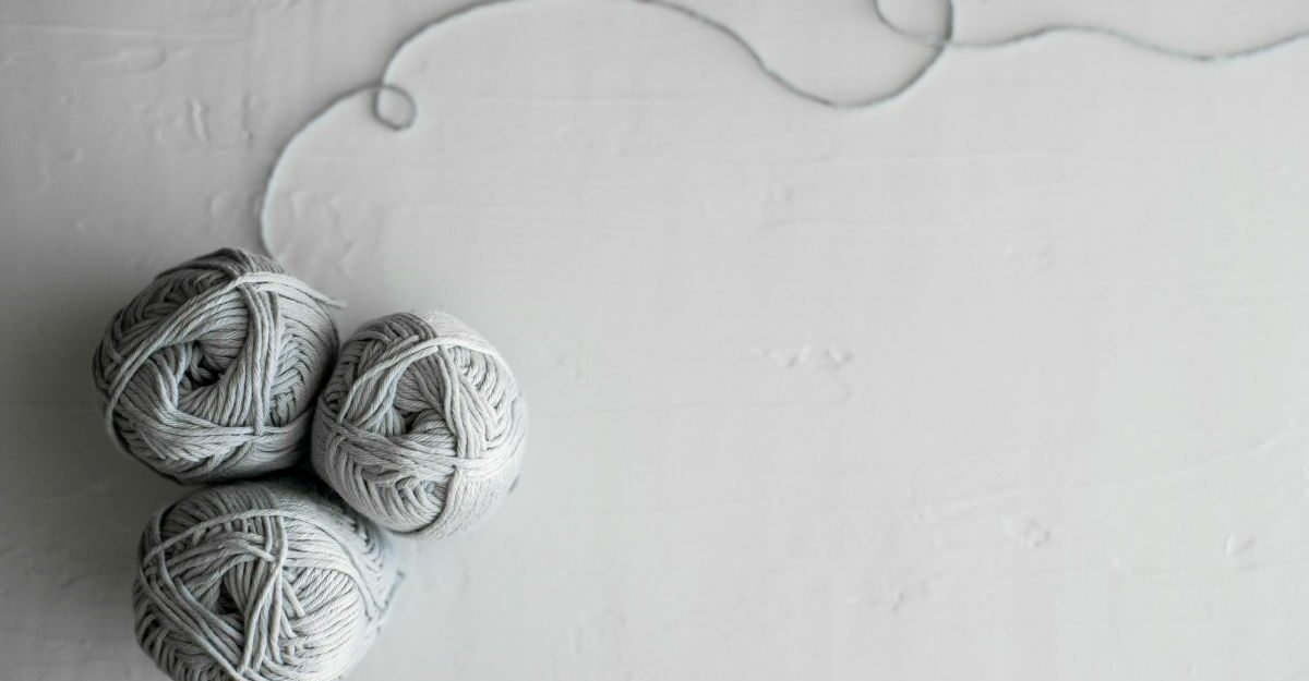Three balls of yarn are clumped together, with a a light grey thread extending from one.