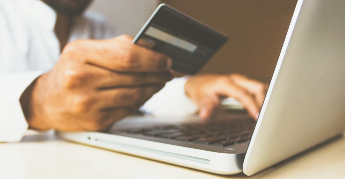 A person holds their credit card as they navigate a purchase on their laptop.