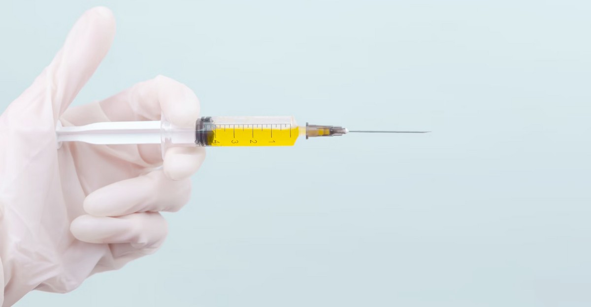 A person holds a syringe with a yellow fluid inside. (Photo: diana_pole / Unsplash)