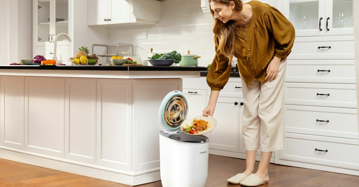 A woman in a bright, modern kitchen emptying food scraps into a countertop food waste bin, illustrating household composting amid news about Convertus layoffs in Canada.