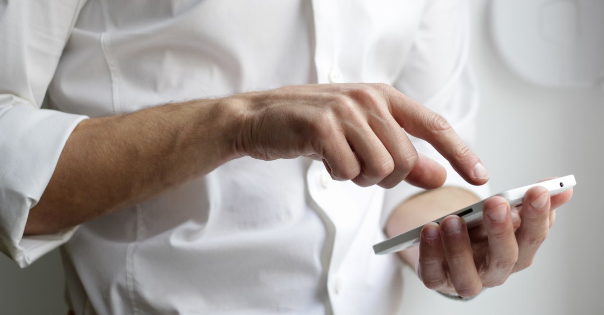 Person wearing a white shirt using a smartphone, representing communication or checking work updates online.