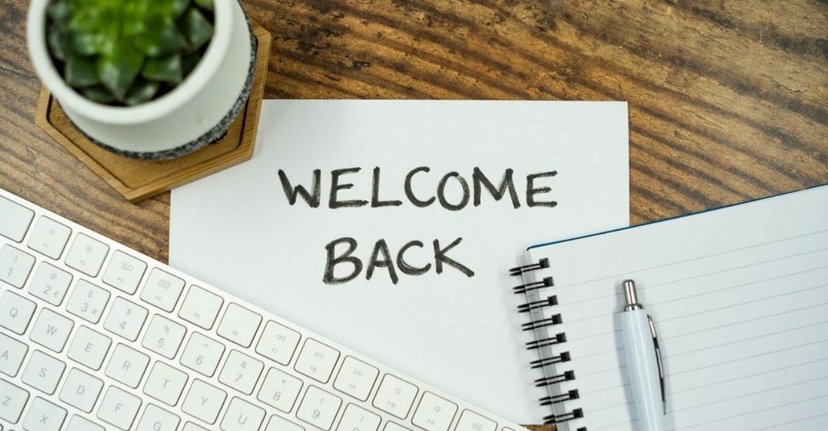 A desk with a keyboard, notebook, pen, and a small plant surrounding a paper sign that says “Welcome Back.”