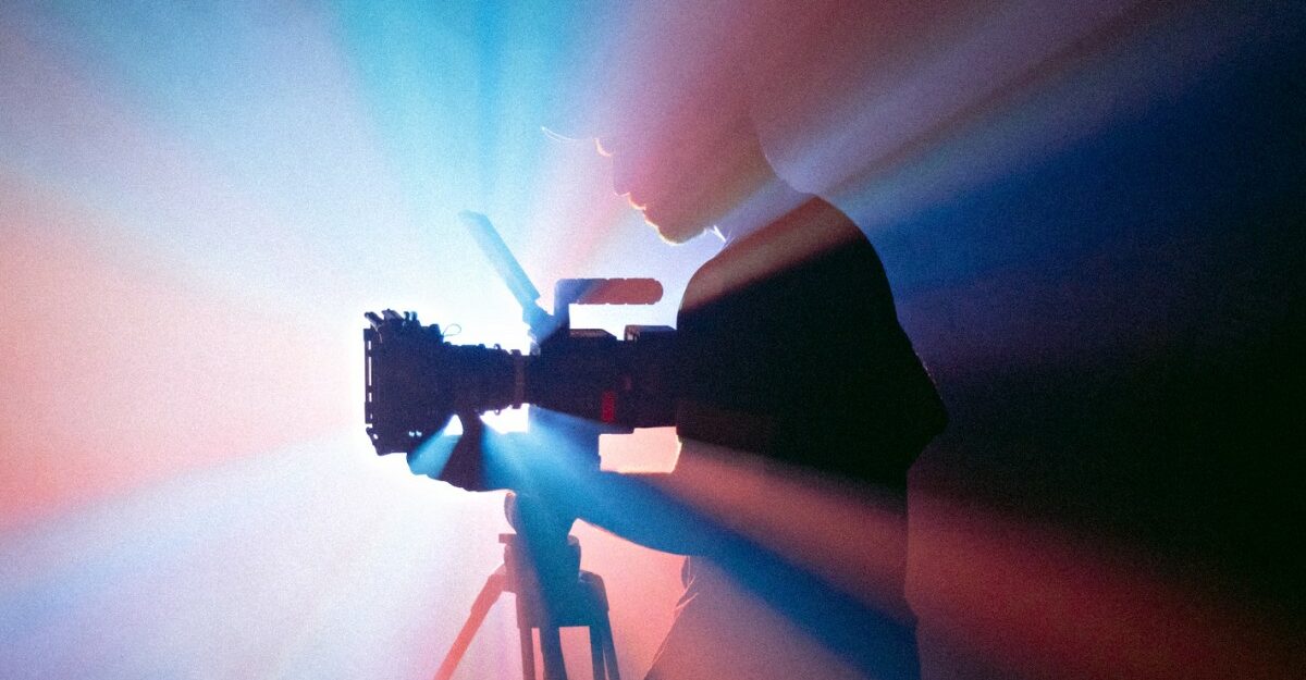 A person examining a camera in front of a projector. (Photo: Jakob Owens / Unsplash)