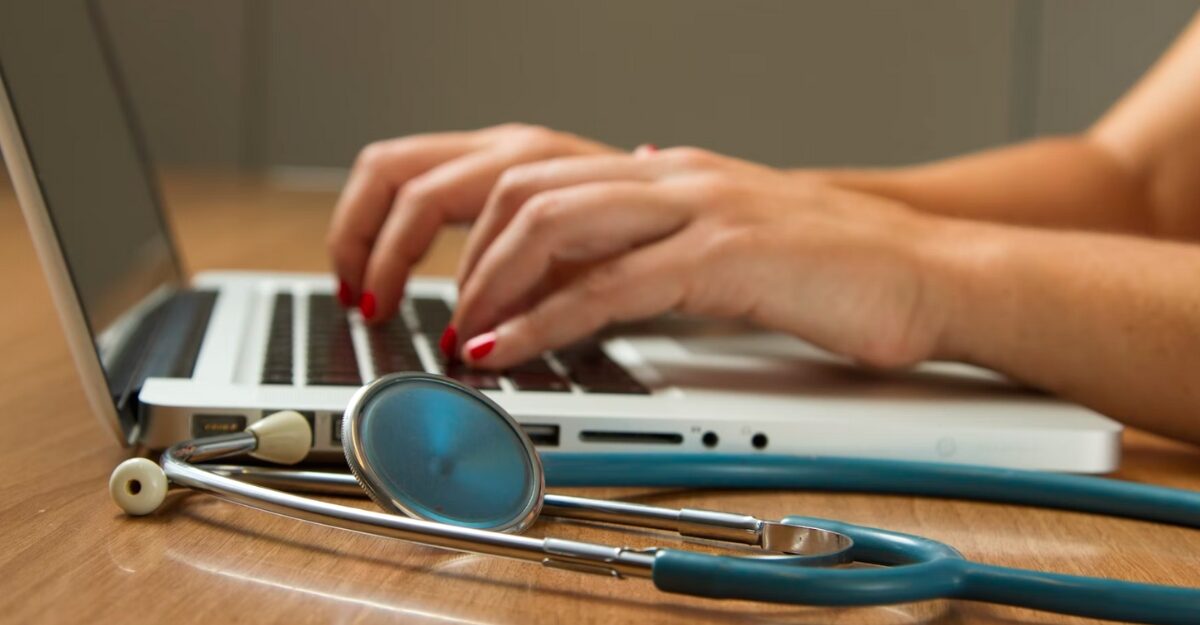 A person uses a laptop with a stethoscope beside them. (Photo: National Cancer Institute / Unsplash)